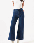 On a white background is a model wearing a dark blue pair of denim jeans with front pockets, a high waist and flair bottoms.