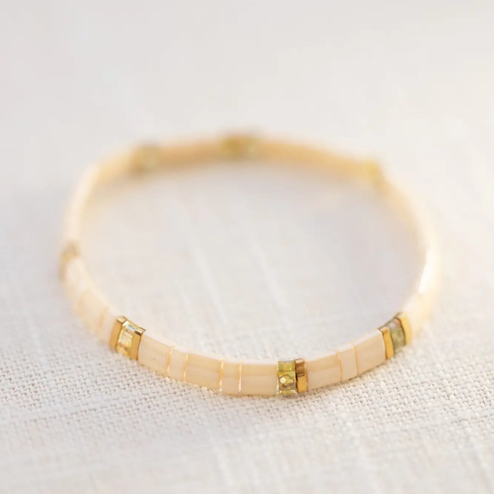 On a neutral background is a light pink and gold beaded bracelet. 
