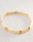 On a neutral background is a light pink and gold beaded bracelet.