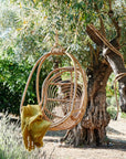 A natural rattan egg shaped hanging chair with an ivory cushion and rope details.
