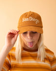 A model wearing the toffee colored baseball cap that has a corduroy texture and says, "San Diego" in white lettering.