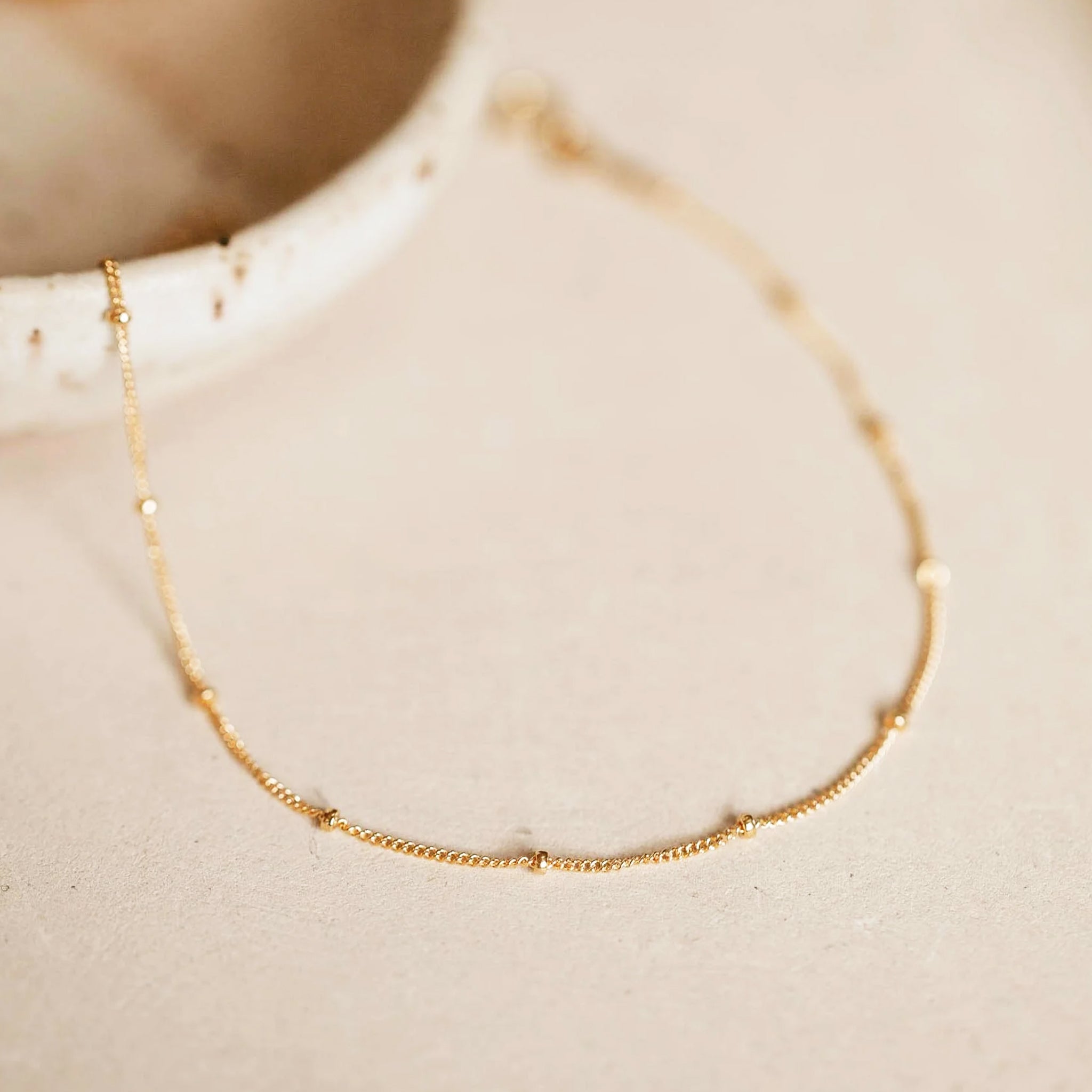 A gold chain anklet with small balls spaced out on the chain. 
