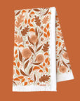 A white cotton kitchen towel with an orange woodland and floral design.