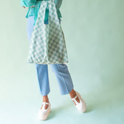 On a light blue background is a model holding a turquoise and light blue checkered print nylon bag.