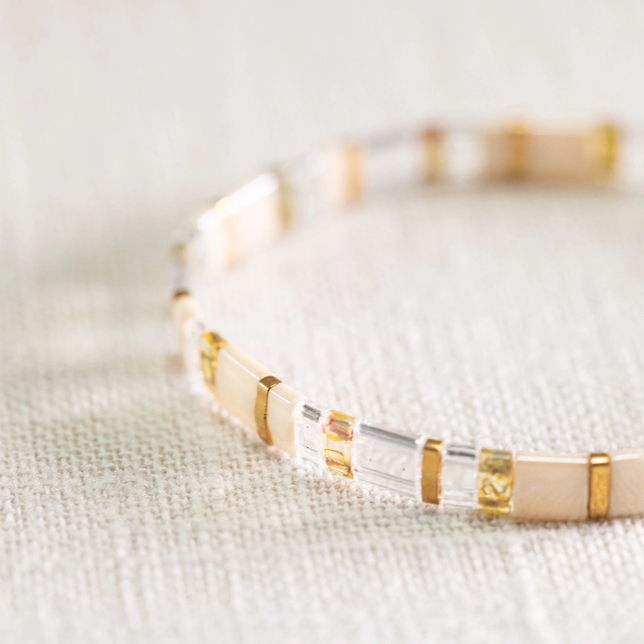 A gold, clear and neutral colored bracelet with a variation of alternating beads.