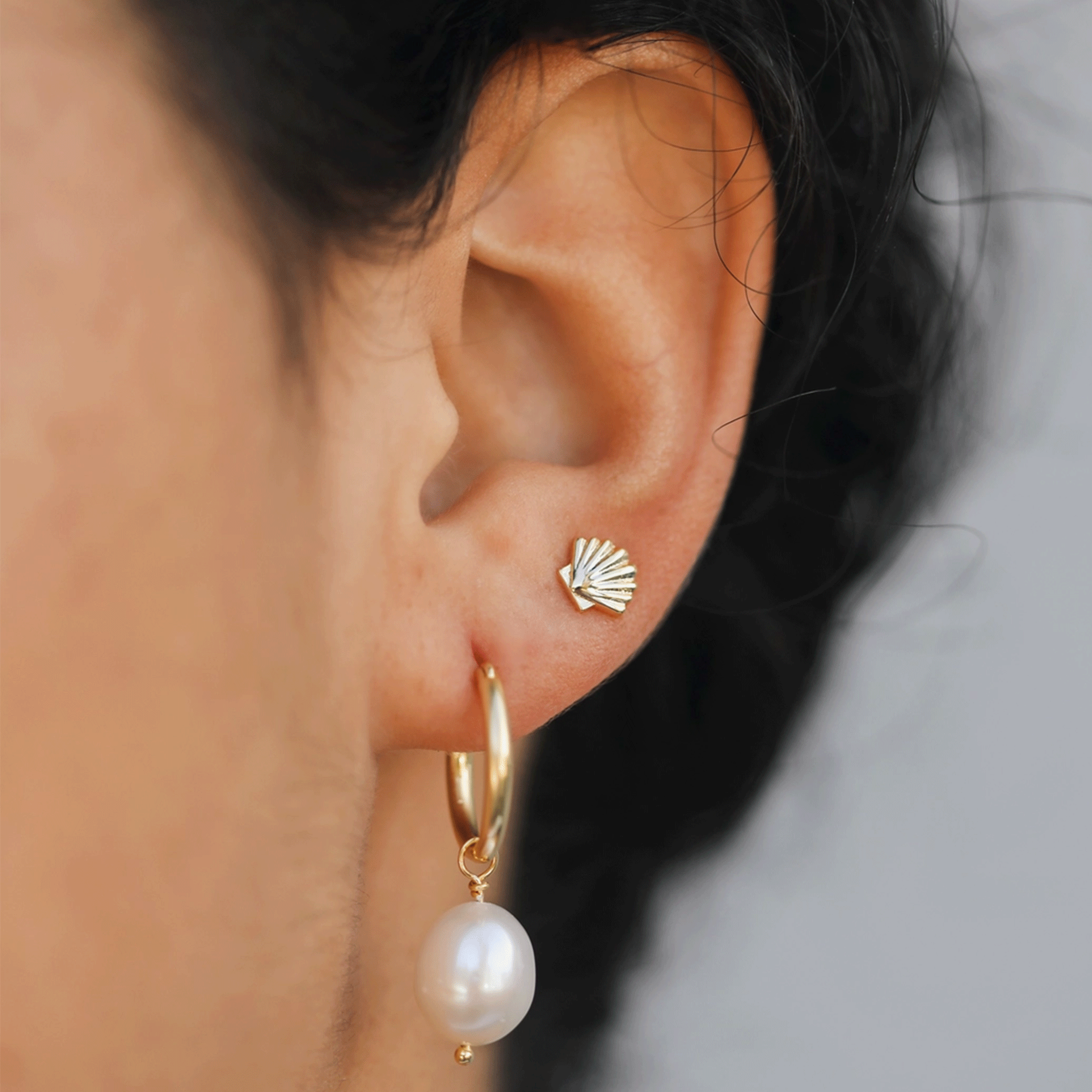 A model wearing the gold seashell shaped stud earring next to a pearl hoop that is not included with purchase. 
