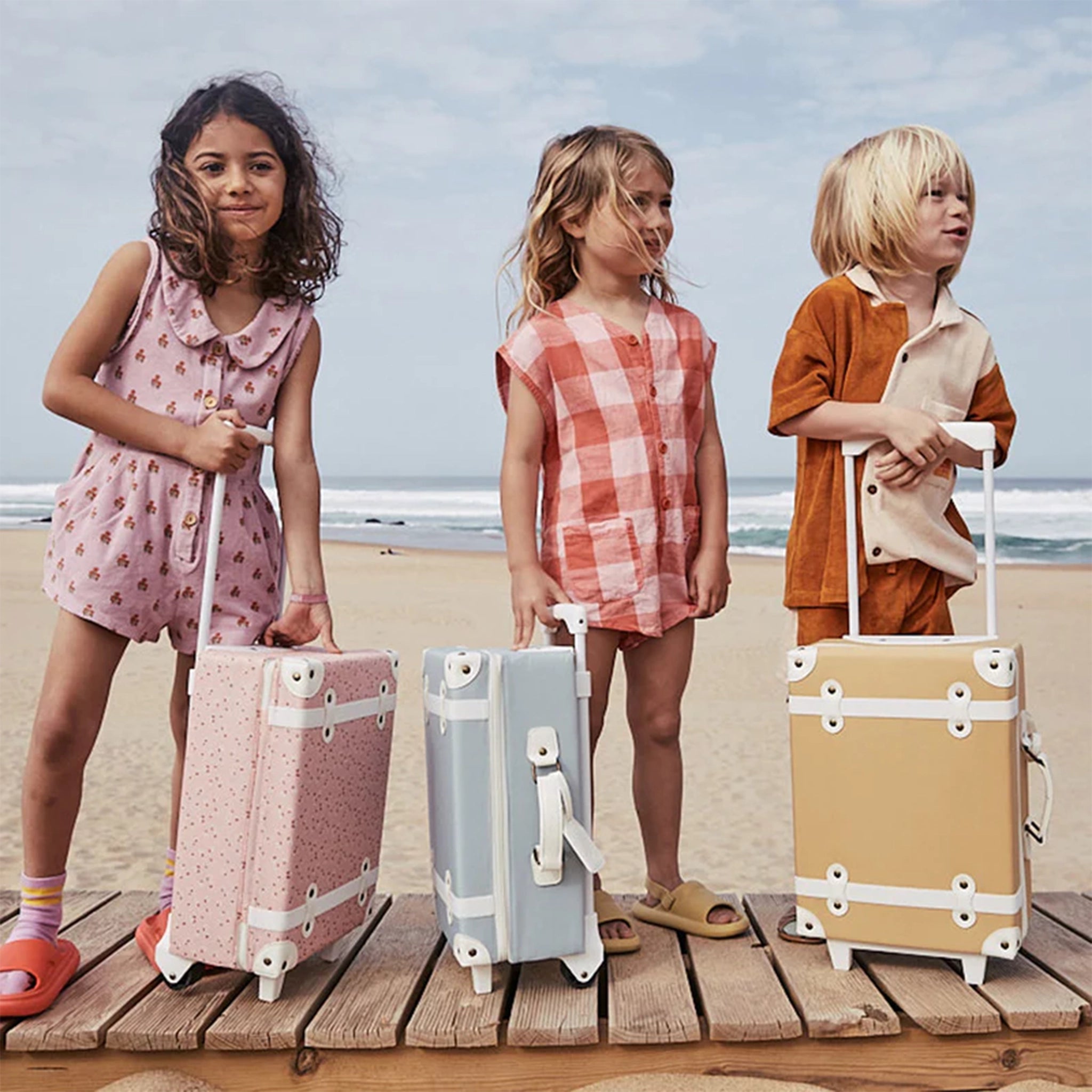 A tan/light orange and white kids suitcase standing next to children models also holding their suitcases. 