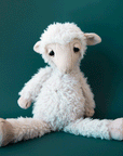 On a teal background is an ivory stuffed animal sheep with sleepy eyes.