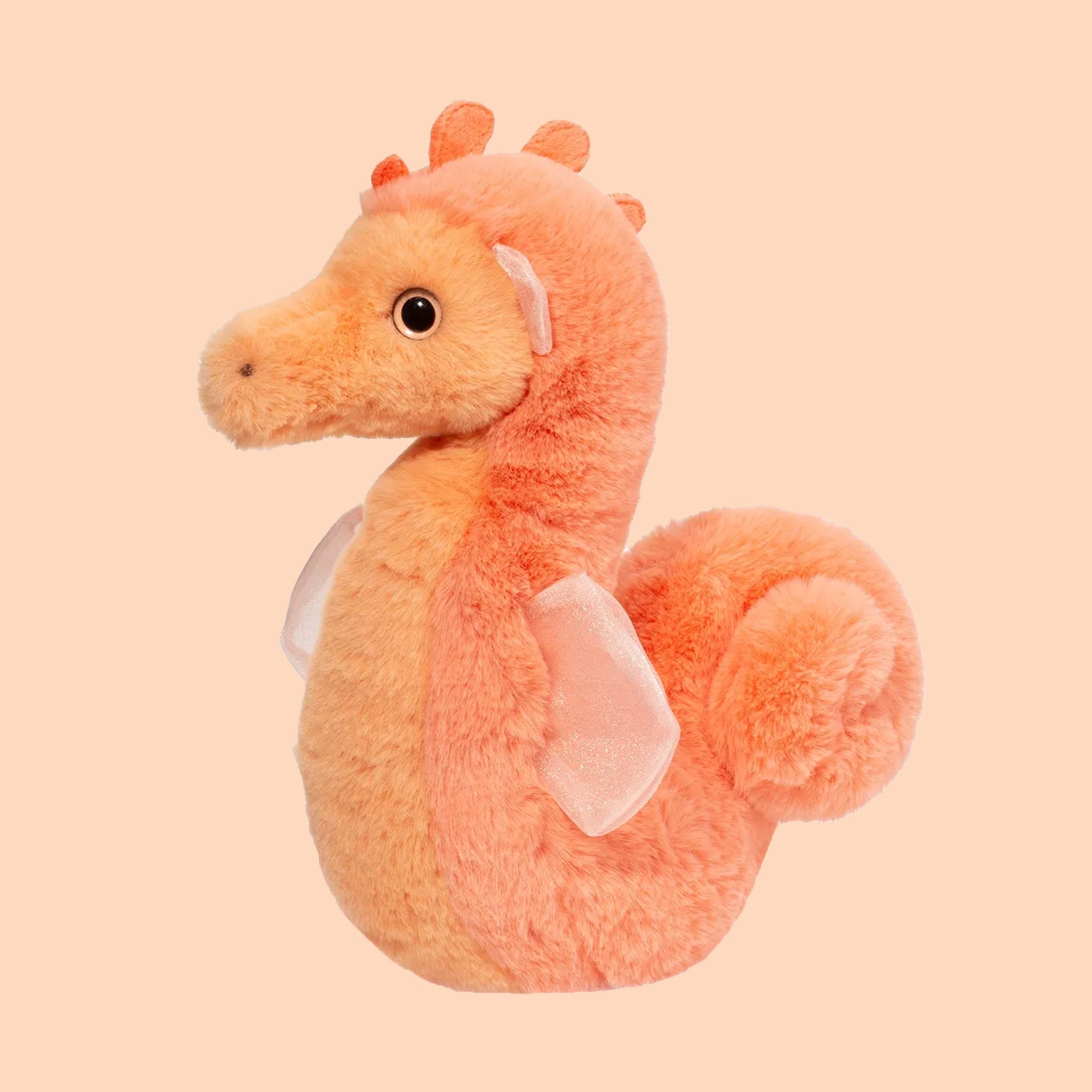 On a peachy background is an orange fuzzy seahorse shaped stuffed toy. 