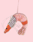 On a pink background is a beaded felt shrimp ornament with diamond details and pink and orange beading.