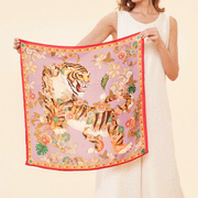 On a tan background is a square silk scarf with a tiger and floral design. 