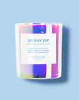 An iridescent glass candle with a white label that reads "Skinny Dip".