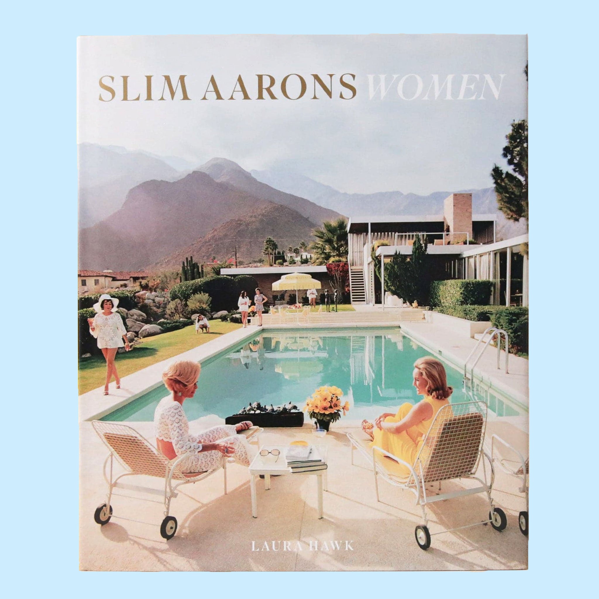 A book cover featuring a photo of 3 women around a pool outside of a midcentury home with a beautiful mountainous background. The title reads, &quot; Slim Aarons Women&quot;.