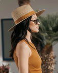 A model wearing a tan woven sun hat with a band around the base of the hat.