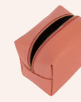 A coral vegan leather toiletry case with a handle on one side and a zipper closure across the top.