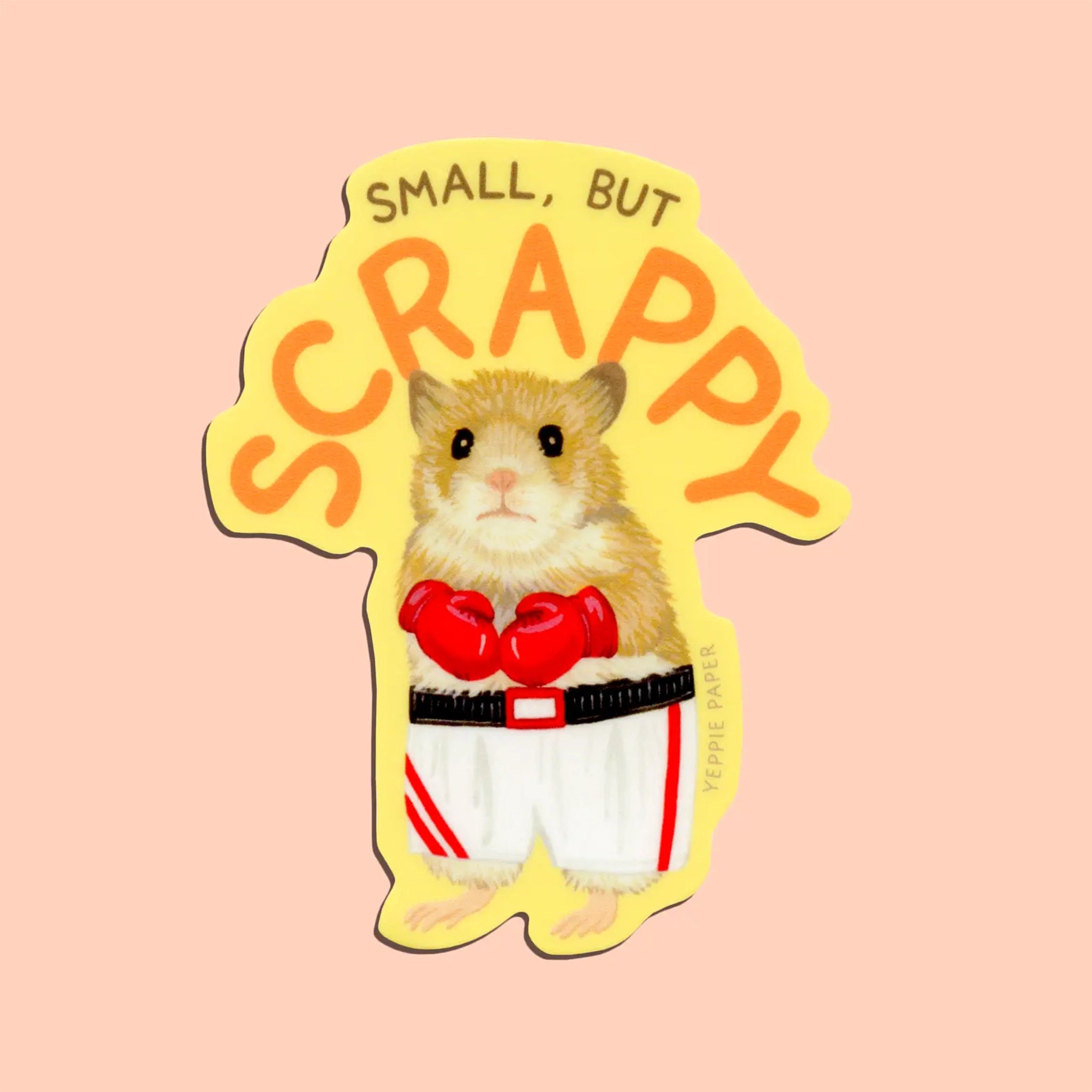 On a peachy background is a light yellow sticker with an illustration of a hamster suited up in boxing gear along with text above it that reads, "Small, but Scrappy".