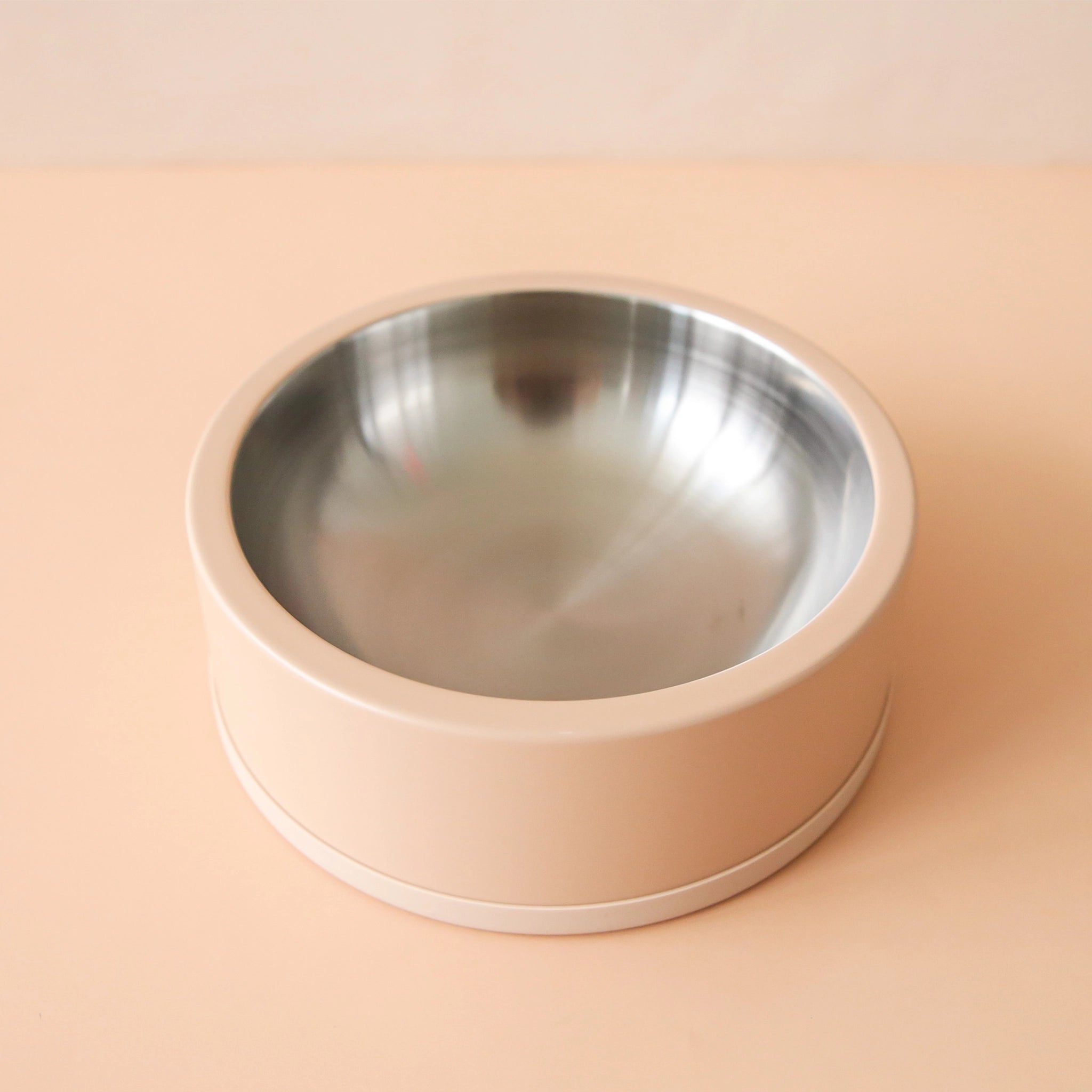 On a peachy background is an arial photograph of a dog bowl with stainless steel interior and a tan exterior.