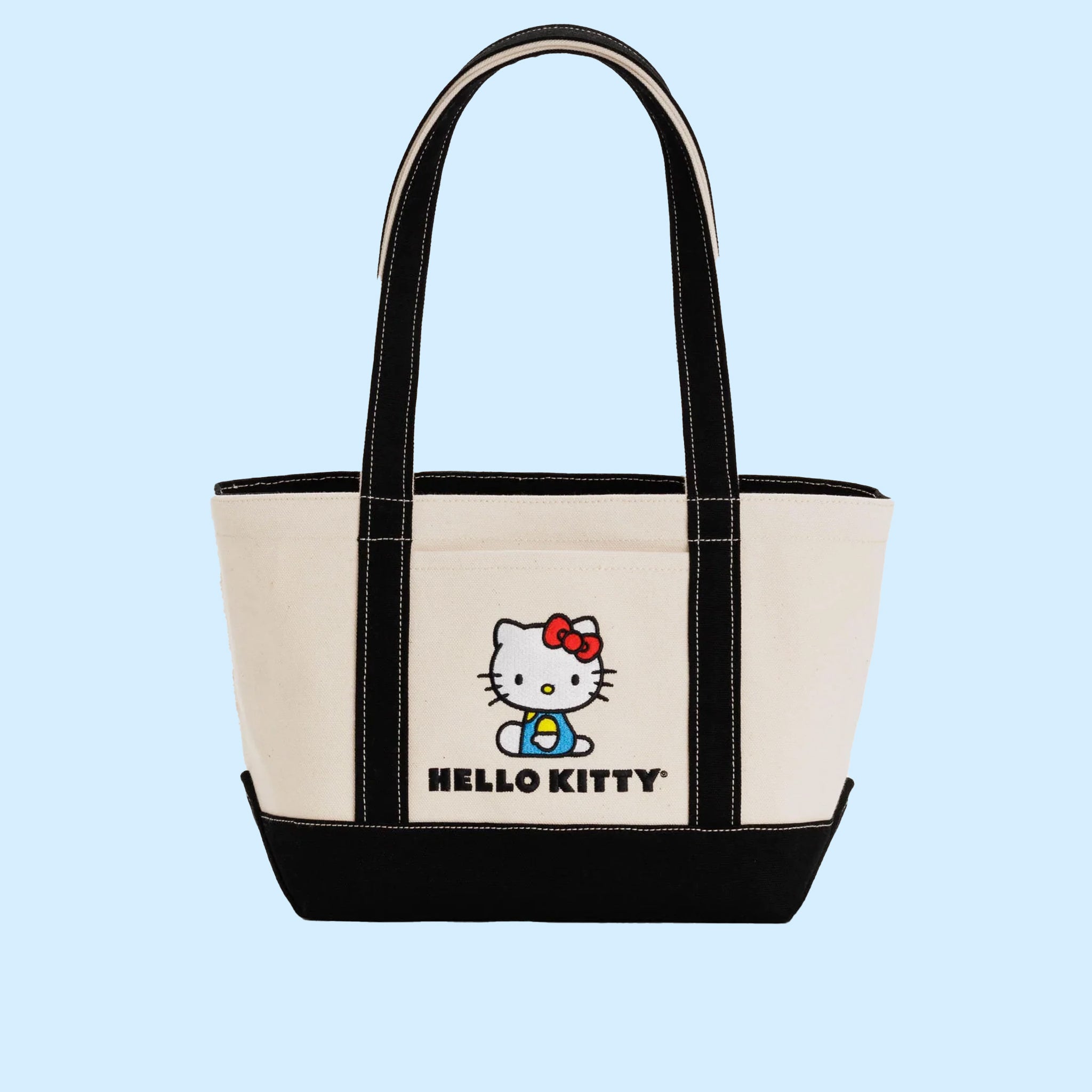 On a light blue background is an ivory and black canvas tote bag with an embroidered graphic of Hello Kitty on the front. 
