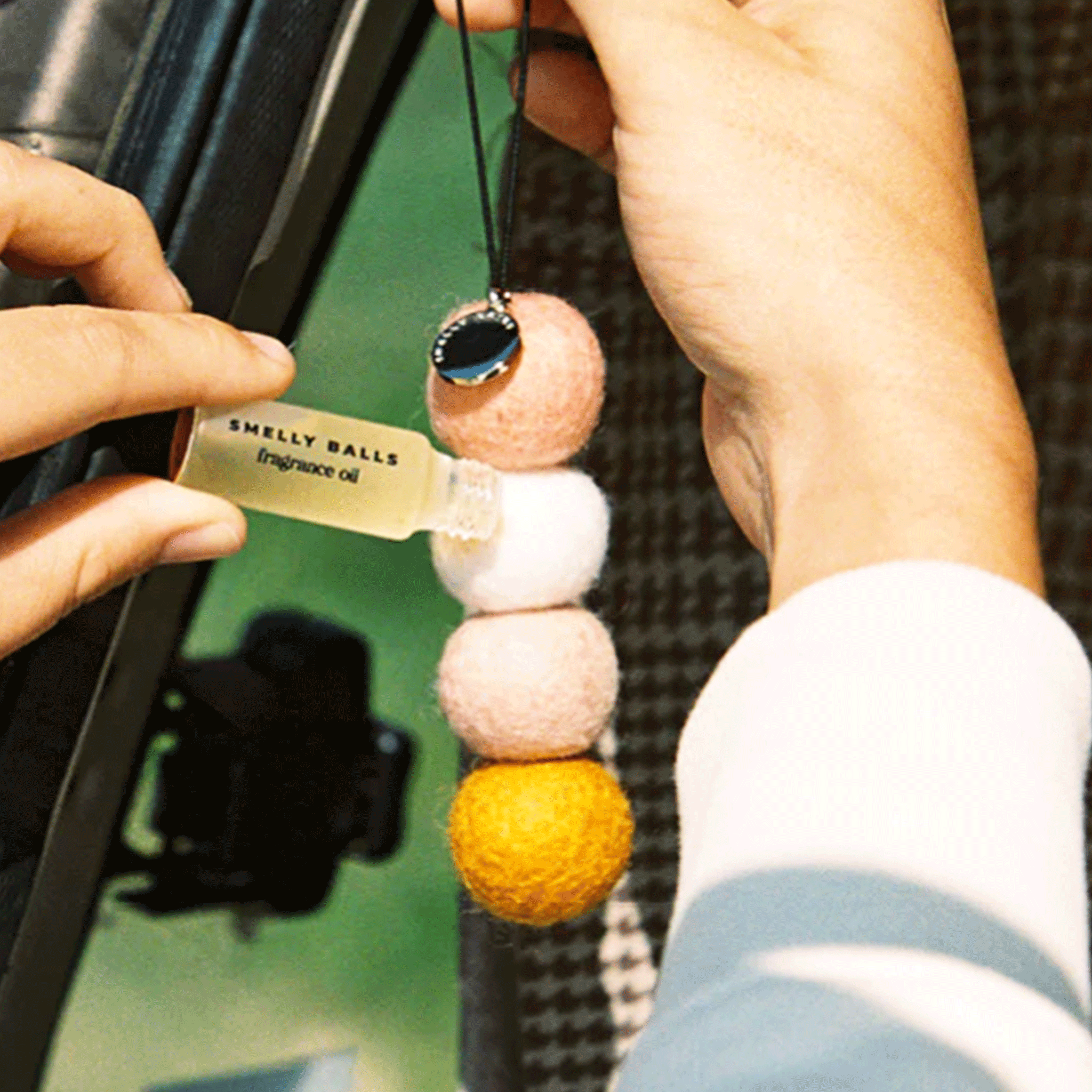 A model holding the four small wool balls made into an air freshener with a small bottle of fragrance oil next to it.