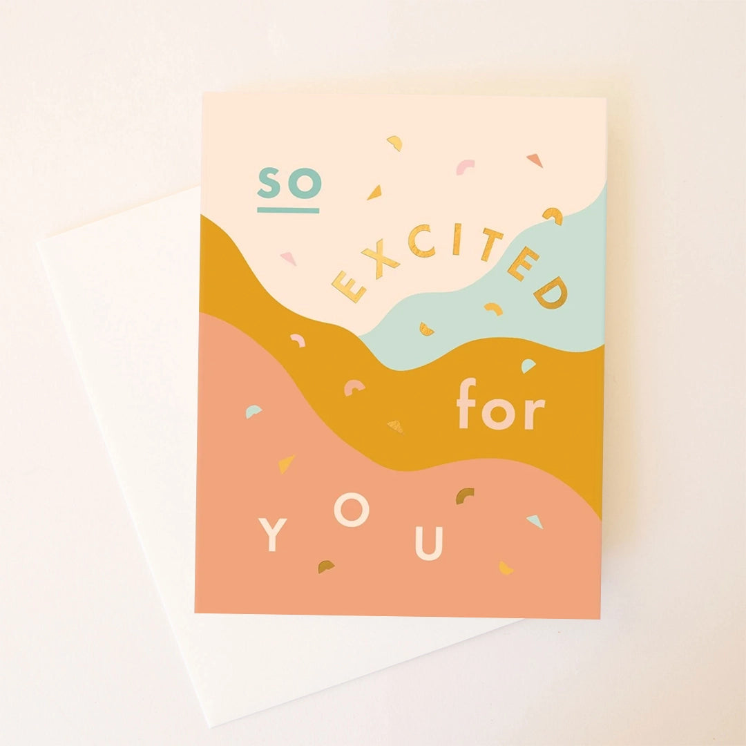 On a white background is a multicolored card with waves that reads, &quot;So Excited for You&quot; in different colored text. 