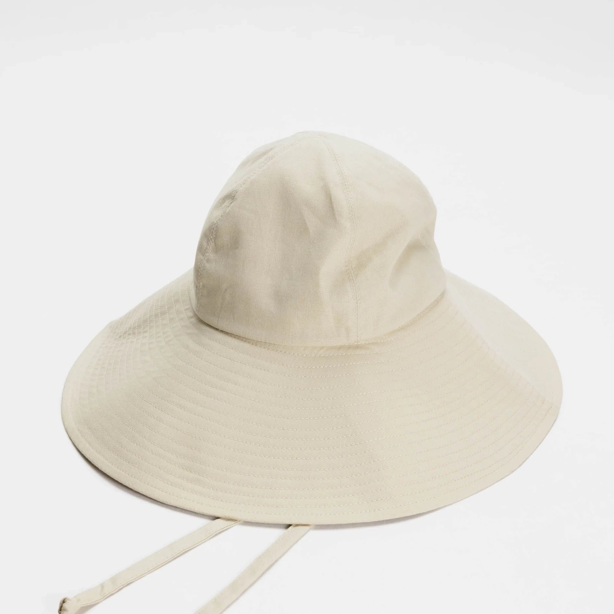 On a white background is a neutral tan soft sun hat with a wide brim a rounded top and neck strings. 