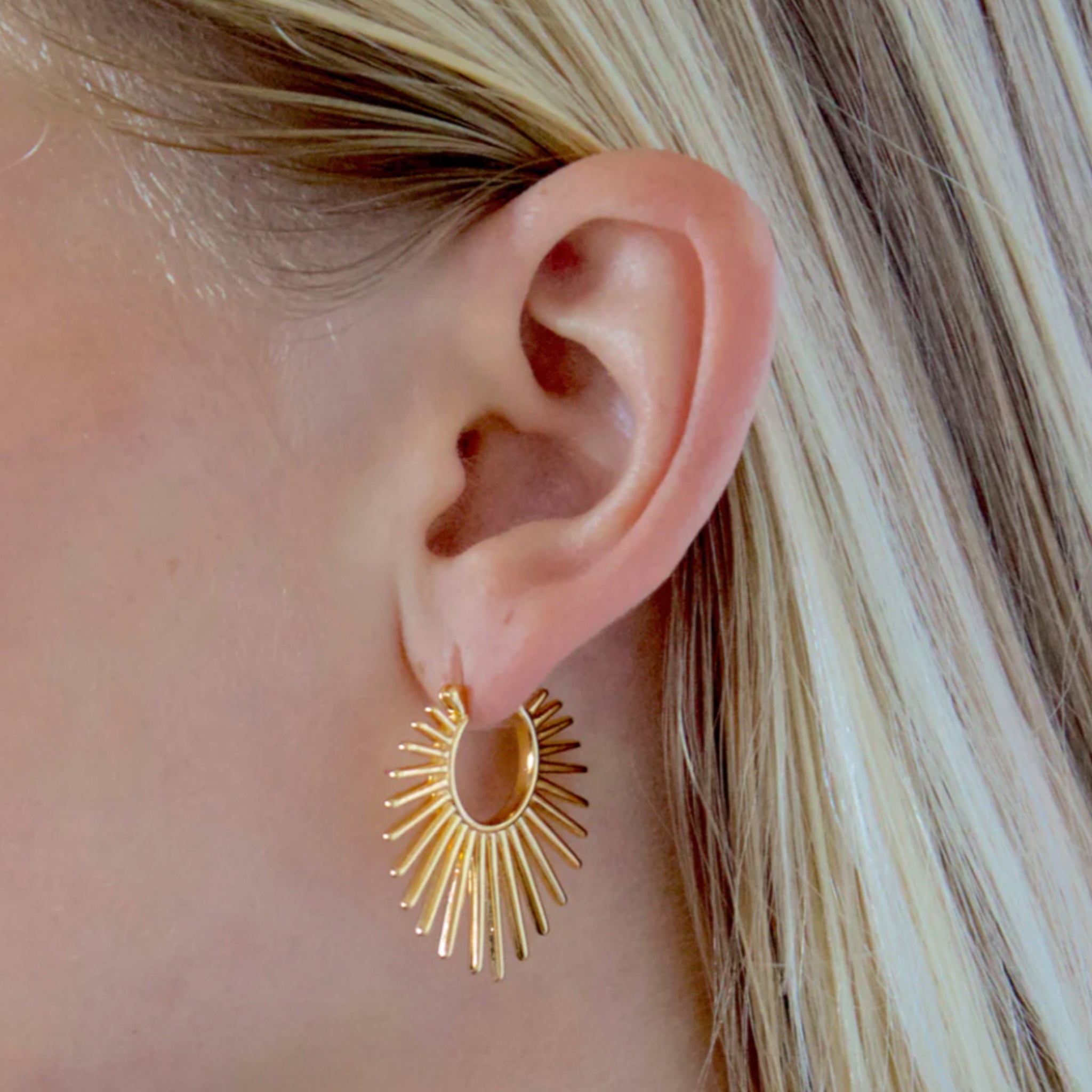 A pair of gold hoop earrings with a sun ray design. 