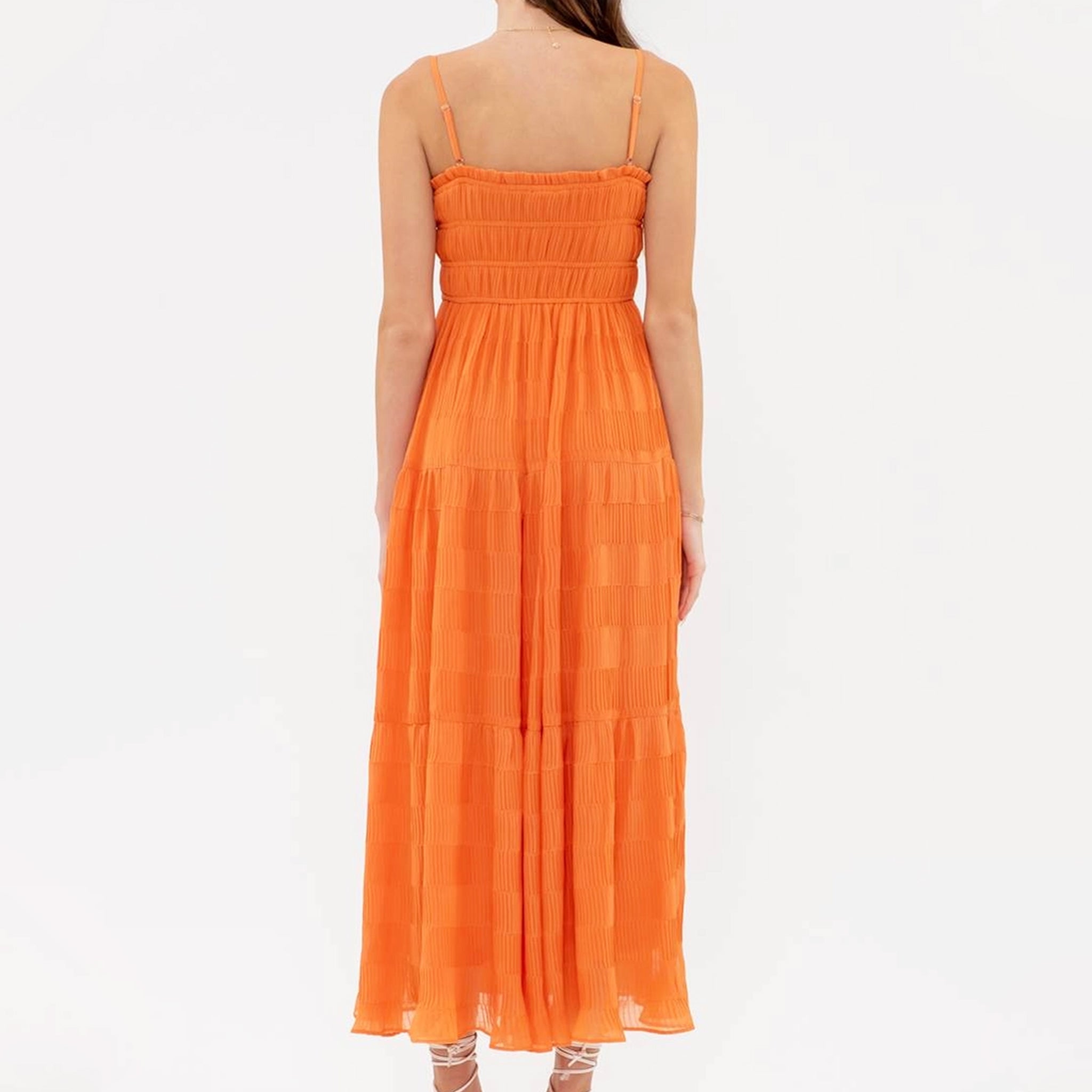 On a peach background is vibrant orange tiered midi dress with a smocked bodice and spaghetti straps.