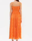 On a peach background is vibrant orange tiered midi dress with a smocked bodice and spaghetti straps.