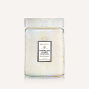 An irridescent embossed glass candle sits in the middle of the image. The label on the glass candle reads, "Sparkling Cuvee"