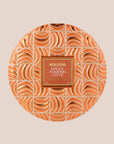 A round orange tin candle with three wicks and text on the lid that reads, 'Voluspa Spiced Pumpkin Latte'.