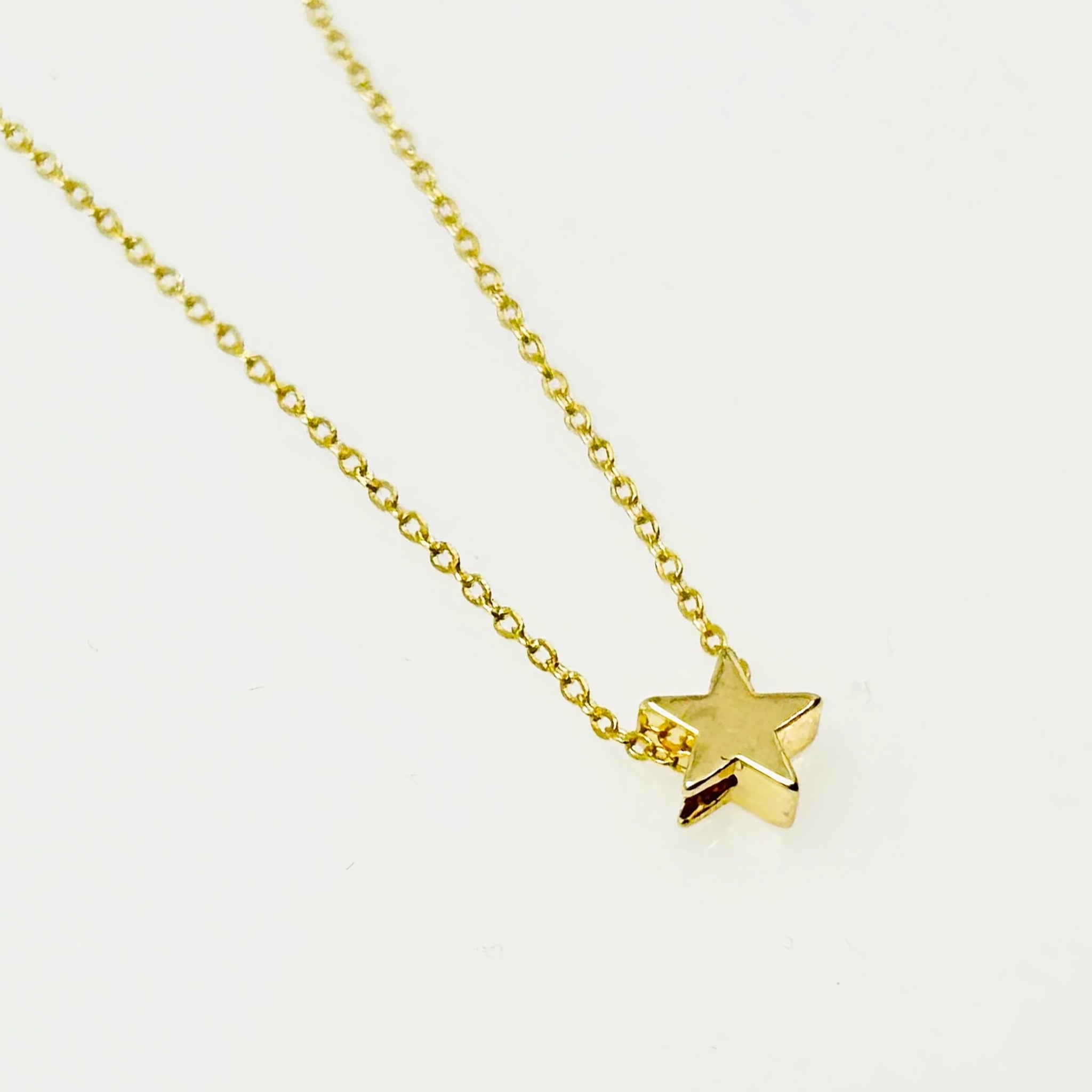 On a white background is a dainty gold chain necklace with a micro star pendant. 