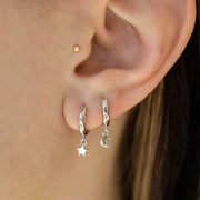 A pair of silver huggie hoop earrings one with a star charm and the other with a moon charm.