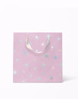 On a white background is a light purple gift bags with a silver star pattern and silver ribbon handles.