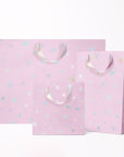 On a white background is three different sized light purple gift bags with a silver star pattern and silver ribbon handles.