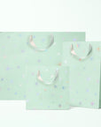 Three different sized mint colored gift bags with silver holographic star patterns and silver ribbon handles.