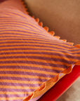 A pink and orange striped pillow with a smaller stripe on the other side and a scalloped edge.