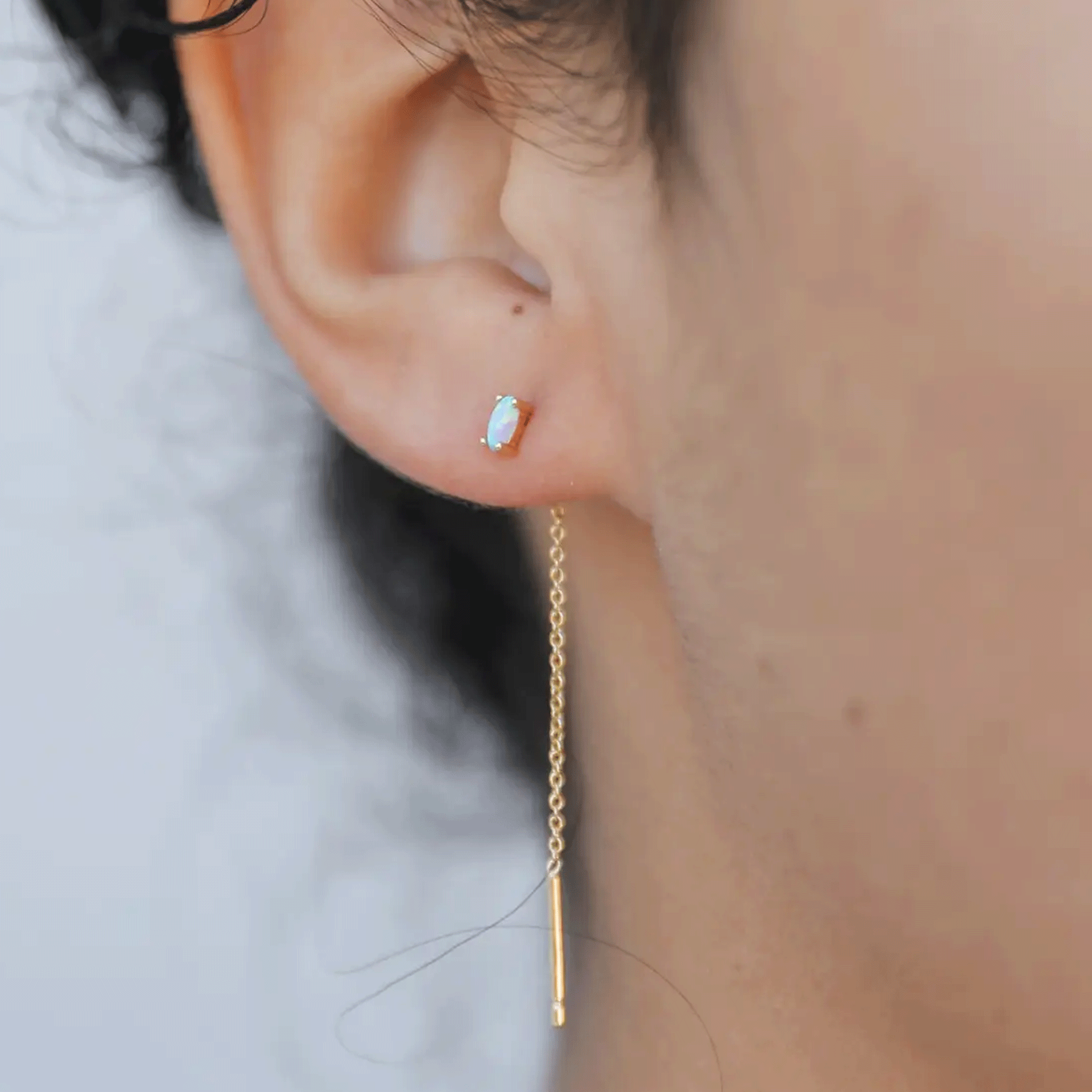 A model wearing a white opal stud with a gold chain thread in the back dangling down.