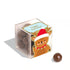 On a white background is a clear acrylic box of chocolate ball candies with a graphic of a cartoon reindeer waving and wearing a red Santa hat along with a speech bubble above that reads, "happy holidays!".