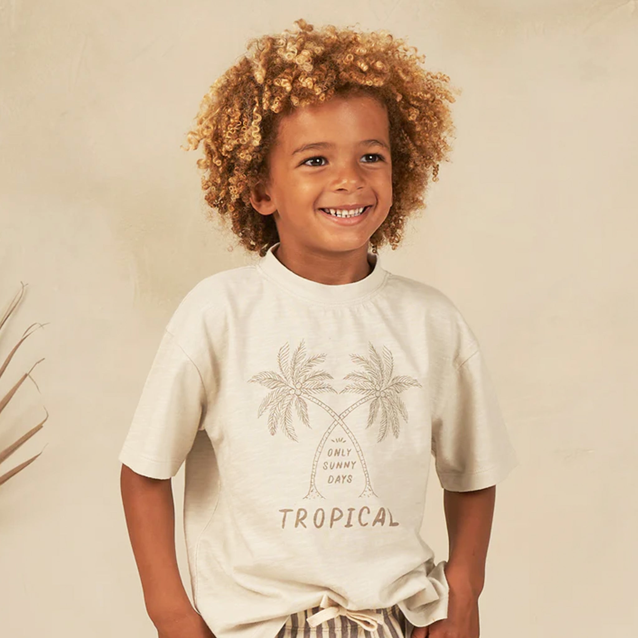 A neutral t-shirt with a palm tree graphic on the front and text in between that reads, "Only Sunny Days Tropical". 