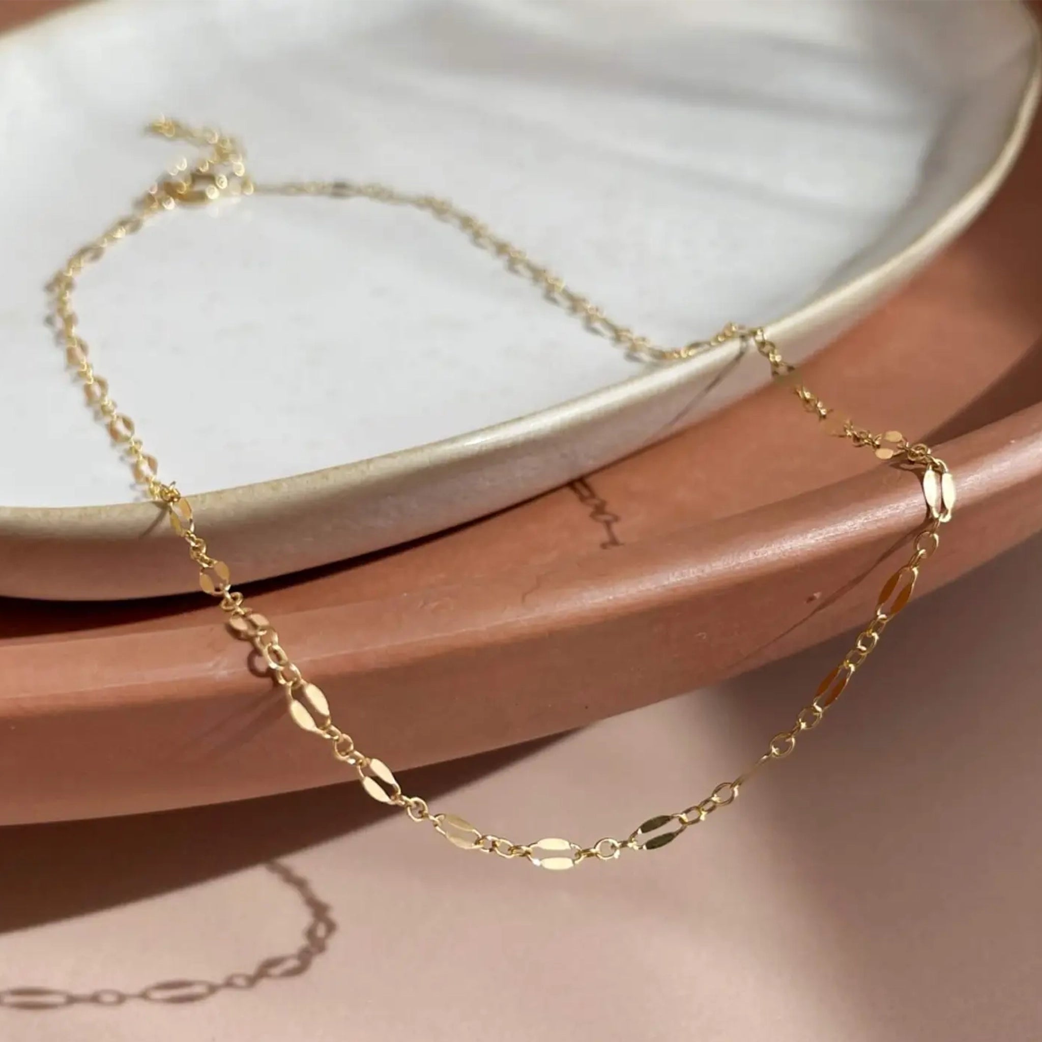 A gold chain choker necklace laying on a ceramic plate. 