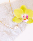 A dainty gold necklace with a single pearl bead in the center.