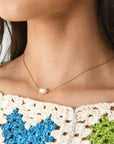 A dainty gold necklace with a single pearl bead in the center.
