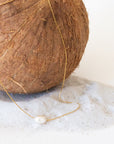 A dainty gold necklace with a single pearl bead in the center.