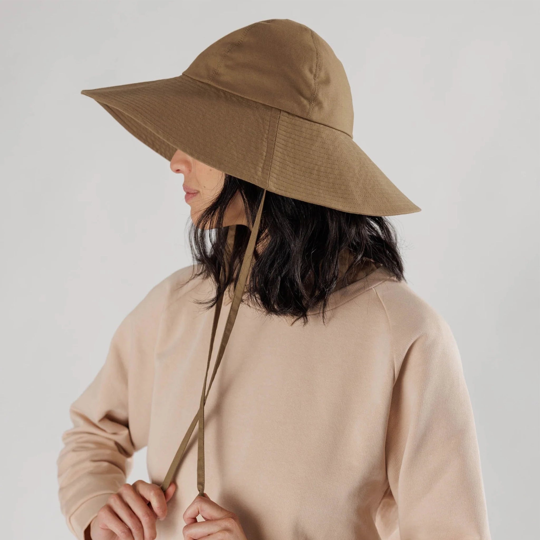 On a white background is a flexible sun hat in a brown shad with a wide brim and two straps for securing around the neck. 