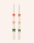 A set of two white taper candles with red, pink and green bow designs.