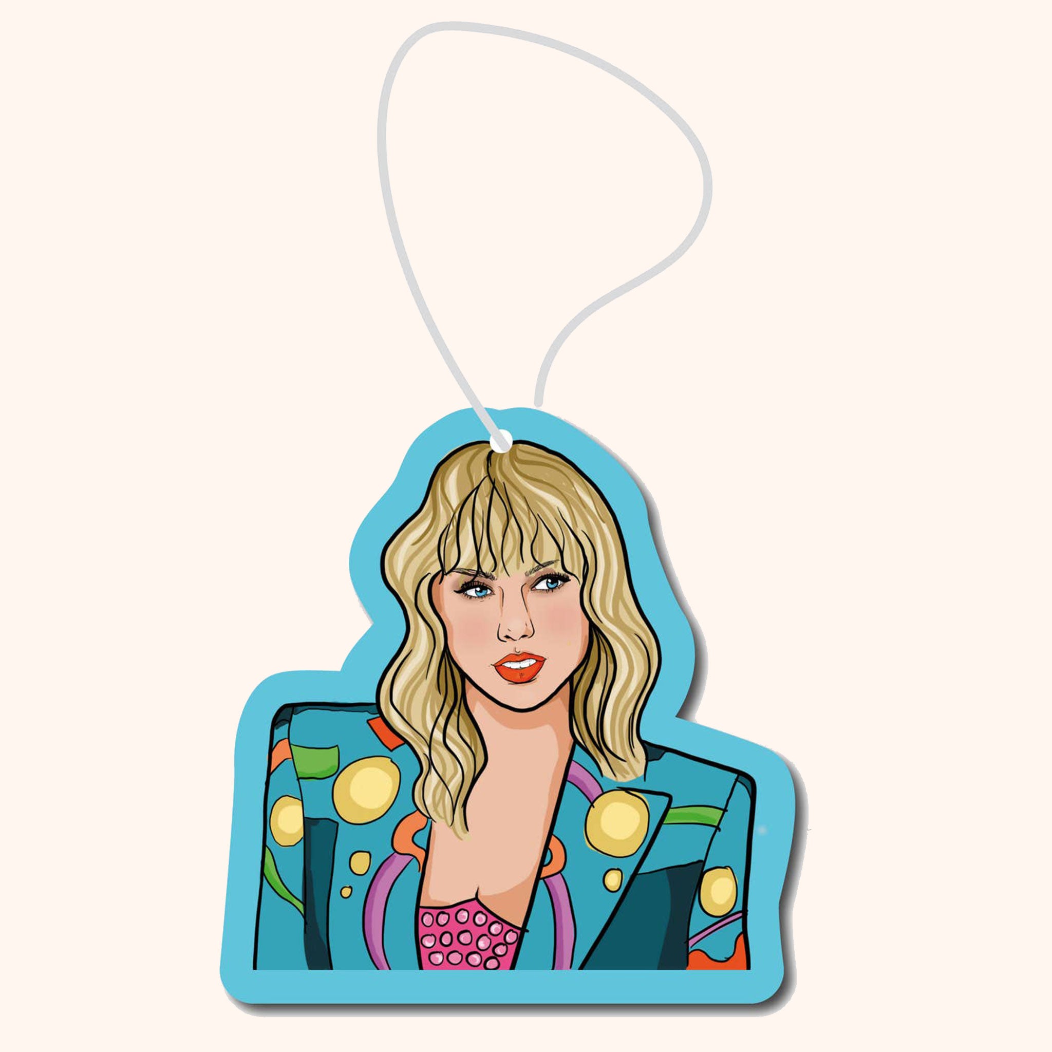 On a neutral background is a car air freshener in the shape of Taylor Swift on a blue background. 