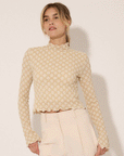 A model wearing a textured ivory top with a floral design and a mock neck that has a subtle ruffle detail.