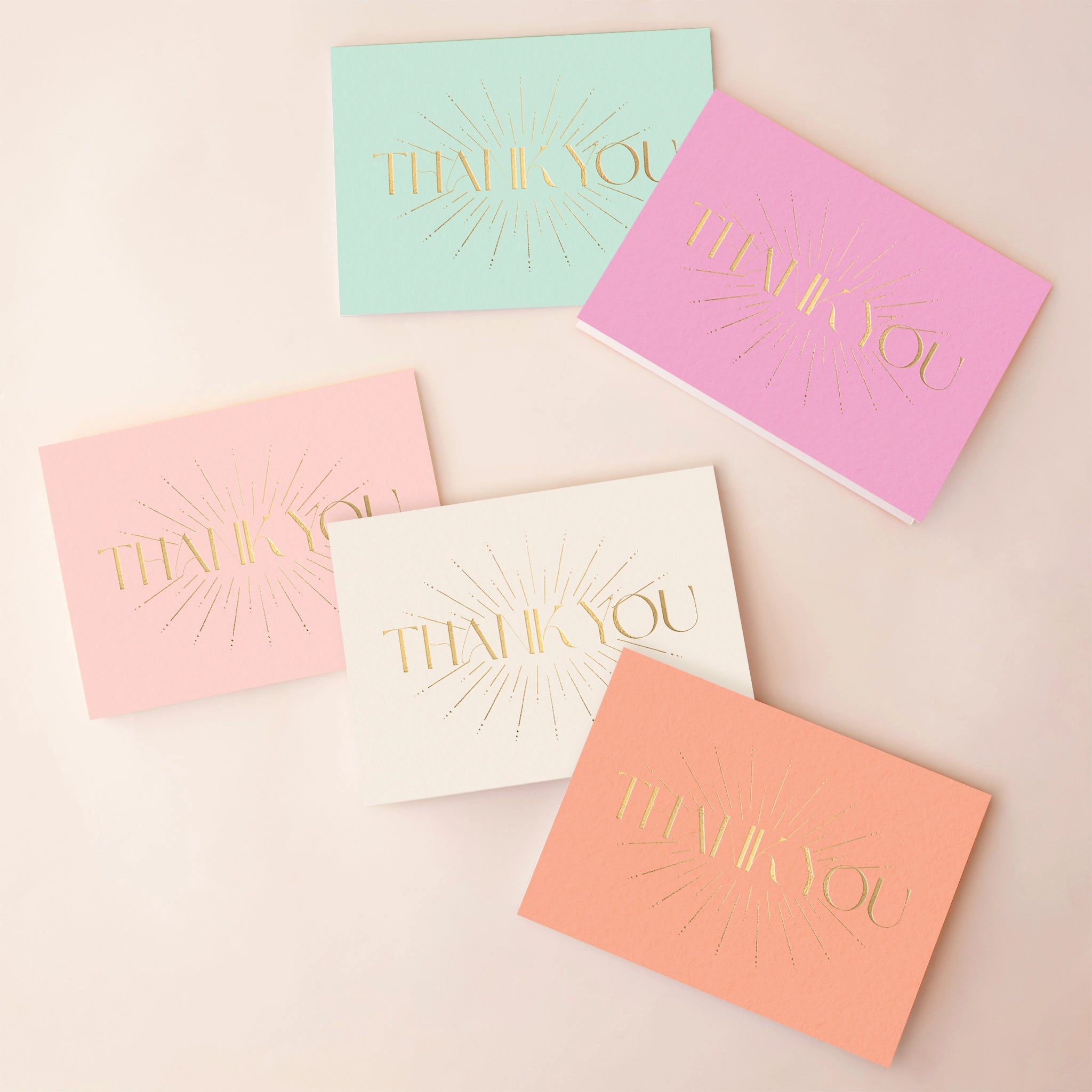 On an ivory background is five different colored thank you cards with gold foiled letters in the center that read, "Thank You". The colors come in fuchsia, mint green, light pink, white and salmon. 