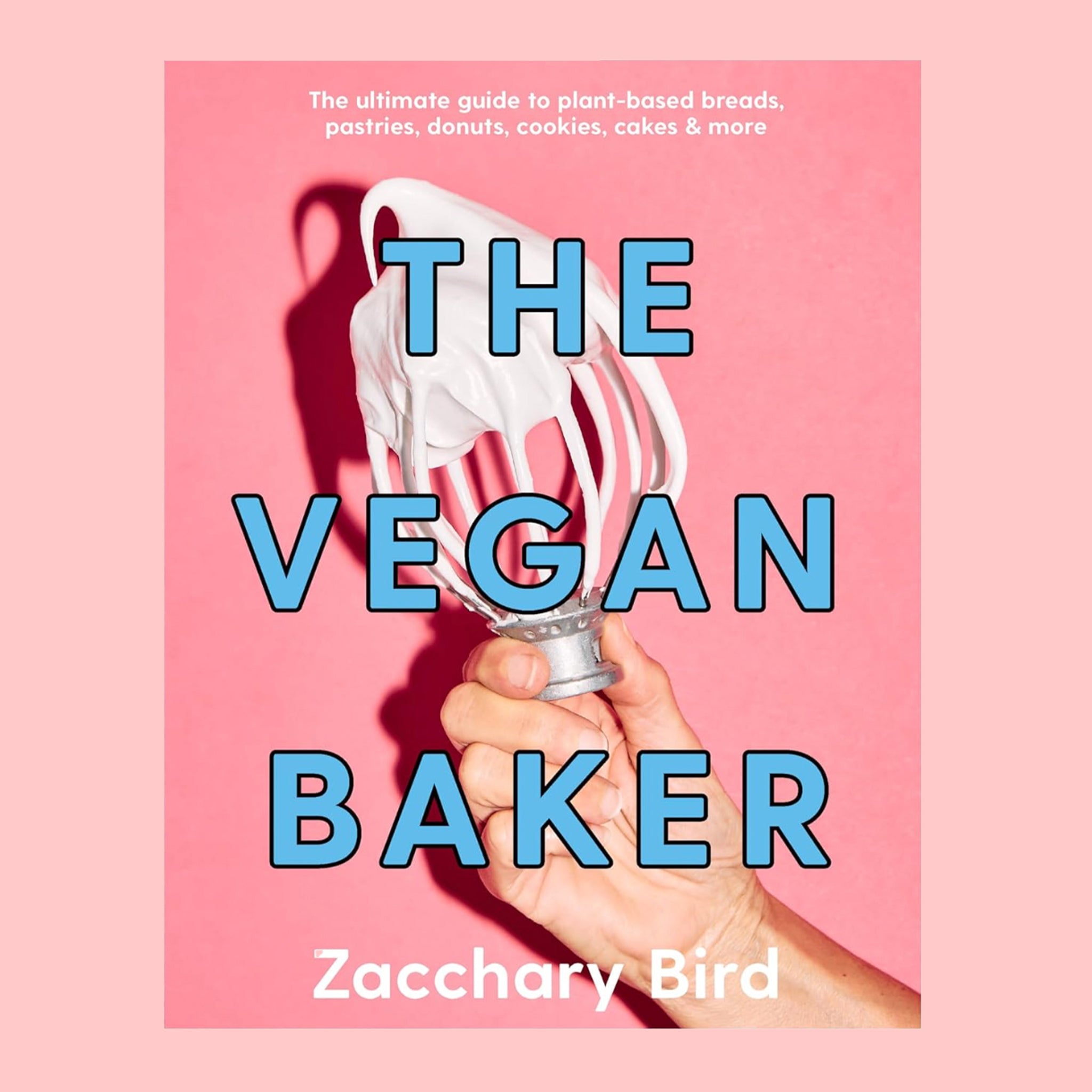 On a pink background is a pink book with a photo of a hand holding a whisk with frosting o it along with blue text in the center that reads, &quot;The Vegan Baker&quot;. 