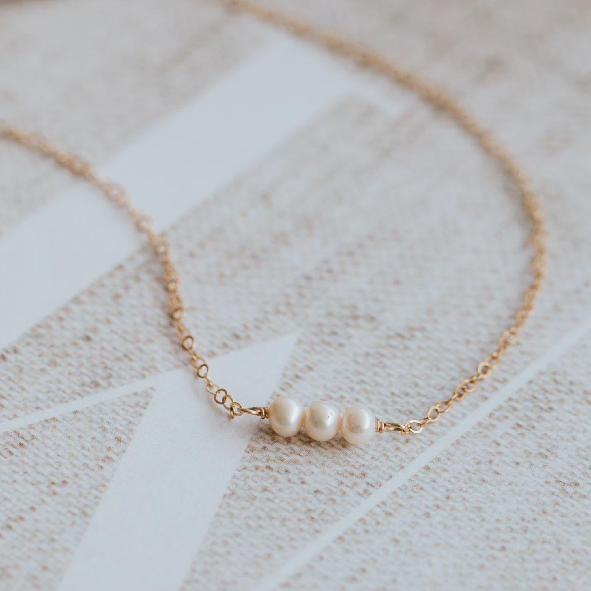 A gold chain necklace with three small pearl connected in the center.